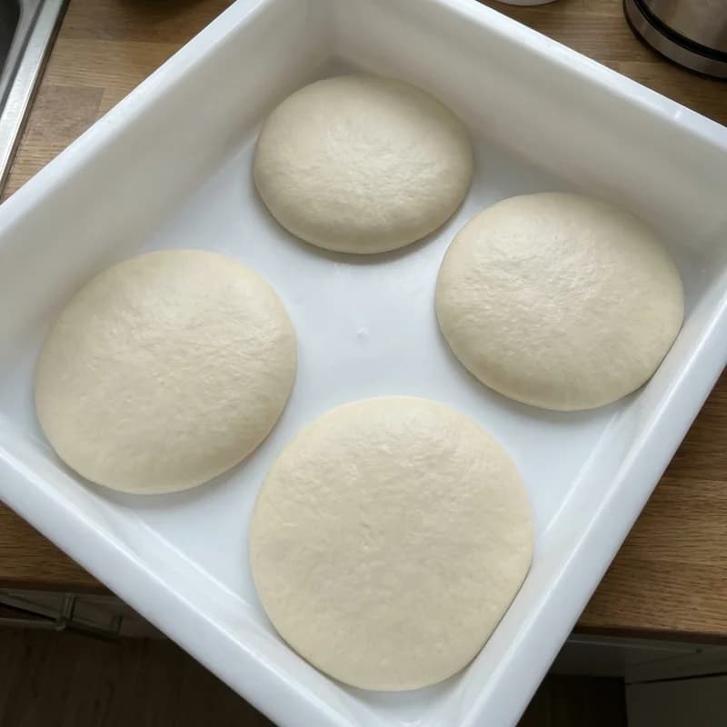 Four wide, flat pizza dough balls in a white container